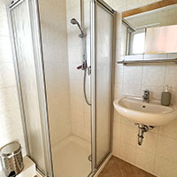 Kleines Badezimmer mit Dusche, Waschbecken, Spiegel und Seifenspender.