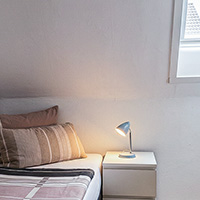 Gemütliches Schlafzimmer mit Doppelbett, gestreiften Kissen und einem kleinen Nachttisch mit einer Leselampe.