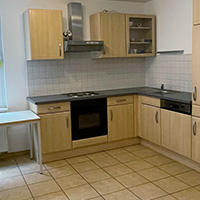 Kleine Küche mit hellen Holzschränken, Herd, Geschirrspüler und kleinem Tisch am Fenster.